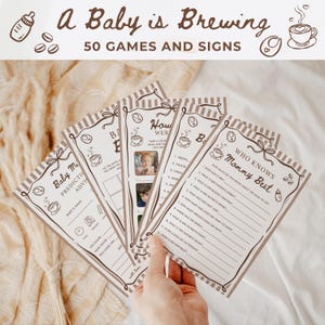 May include: A set of printed baby shower game cards with brown and white striped borders and coffee-themed illustrations. The cards feature text including A Baby is Brewing, 50 Games and Signs, Baby Milestone Predictions, and Who Knows Mommy Best.