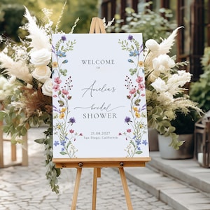 May include: A white welcome sign with a floral border and the text "Welcome to Amelia's Bridal Shower 21.08.2027 San Diego, California".