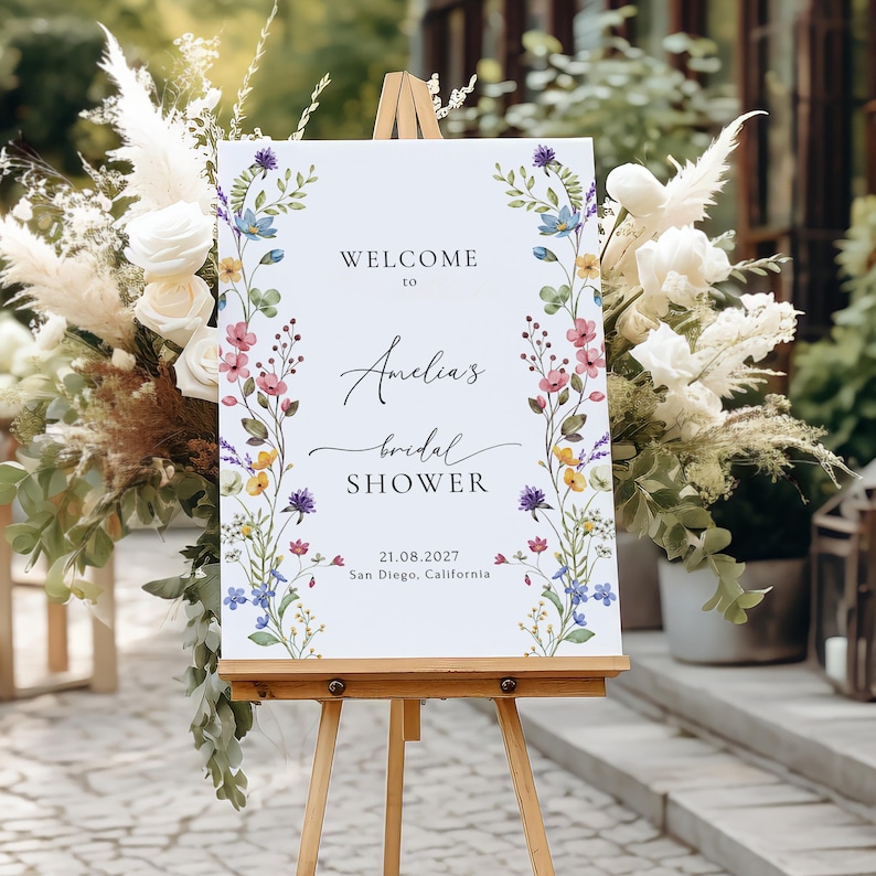May include: A white welcome sign with a floral border and the text "Welcome to Amelia's Bridal Shower 21.08.2027 San Diego, California".