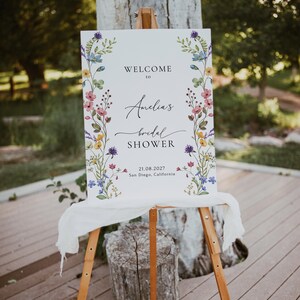 May include: A white welcome sign with a floral border and the text "Welcome to Amelia's Bridal Shower 21.08.2027 San Diego, California".