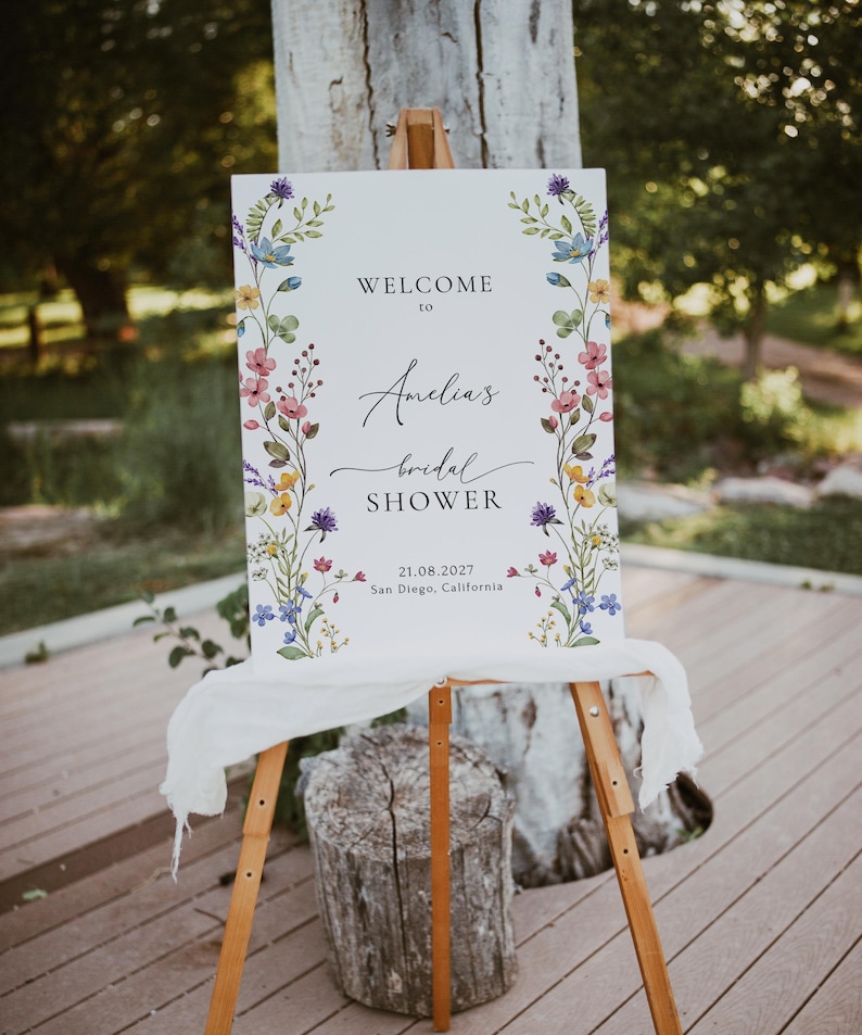 May include: A white welcome sign with a floral border and the text "Welcome to Amelia's Bridal Shower 21.08.2027 San Diego, California".
