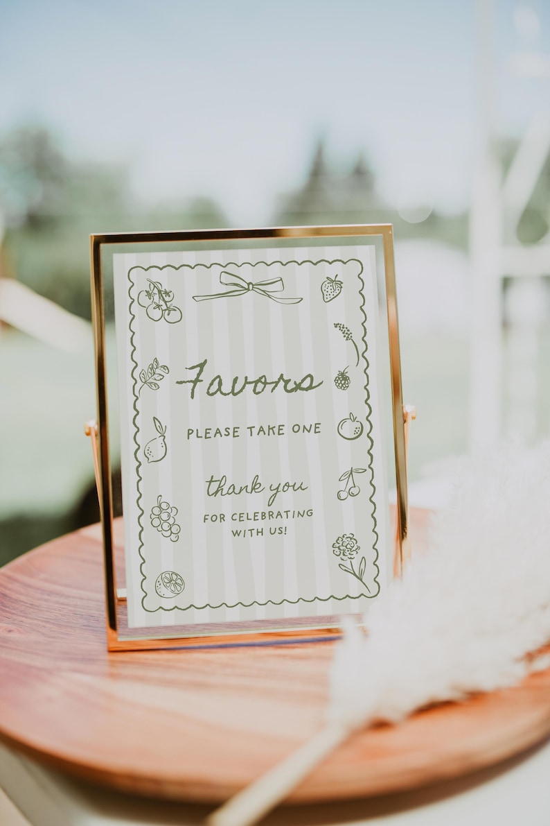 K&ouml;nnte beinhalten: Ein goldgerahmtes Schild mit dem Wort "Favors" in Schrift, umgeben von einem gewellten Rand mit Fruchtdarstellungen. Das Schild lautet "Please take one" und "thank you for celebrating with us!" auf gestreiftem Hintergrund.