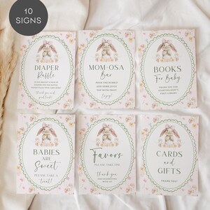 May include: A set of six baby shower signs with a bunny theme. Each sign has a floral border and a watercolor illustration of a bunny. The signs include text such as "Diaper Raffle" and "Mom-osa Bar".