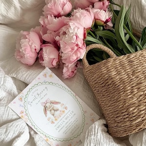 May include: A baby shower invitation with the text "a little Sweet Bunny is on the way" and a watercolor illustration of a bunny. Pink peonies and a woven basket are also in the image.