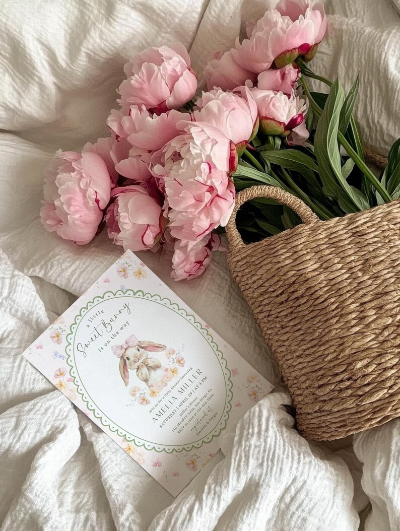 May include: A baby shower invitation with the text "a little Sweet Bunny is on the way" and a watercolor illustration of a bunny. Pink peonies and a woven basket are also in the image.