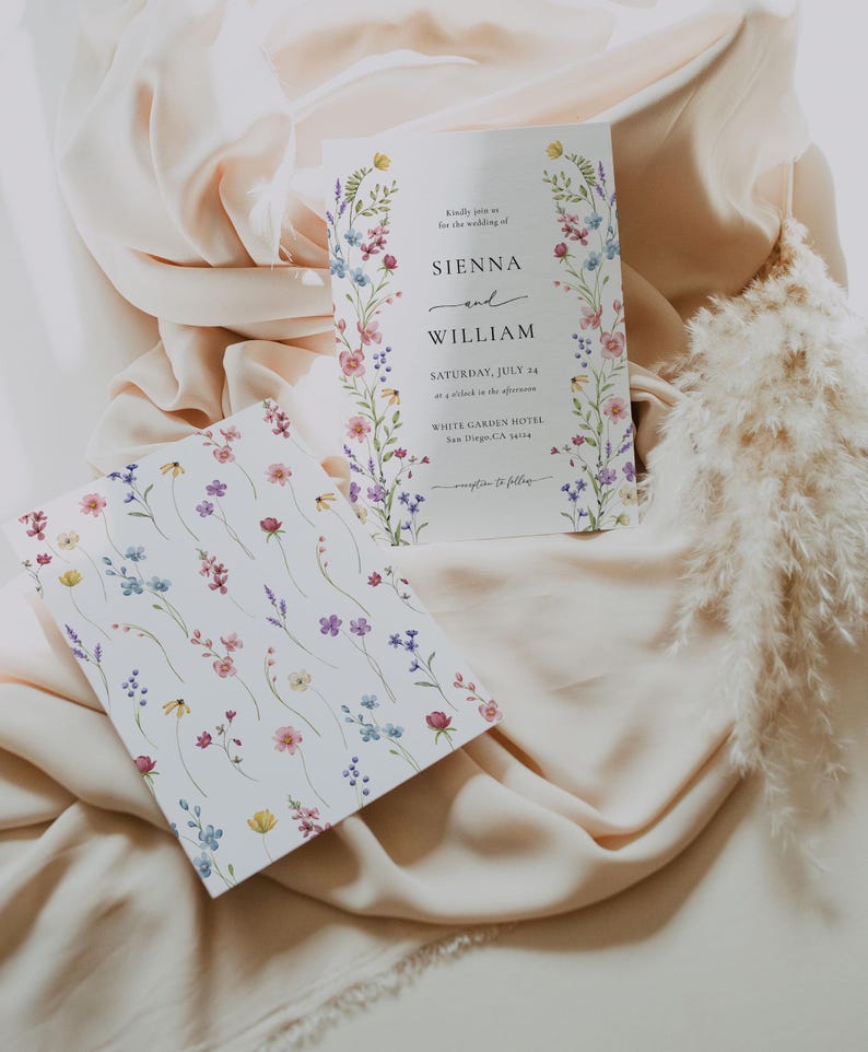 Puede incluir: Invitaci&oacute;n de boda con borde floral y tarjeta a juego. La invitaci&oacute;n dice "Sienna y William" con detalles del evento. La segunda tarjeta tiene un patr&oacute;n floral. Ambas tarjetas est&aacute;n sobre una tela color crema.
