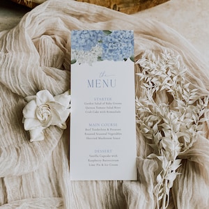 May include: A rectangular menu card with a floral design featuring blue and white hydrangeas at the top. The menu includes starters, main courses, and desserts. The text "the MENU" is written in a delicate script.