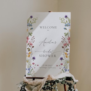 May include: A white sign with a floral border and the text "Welcome to Amelia's bridal shower 21.08.2027 San Diego, California".