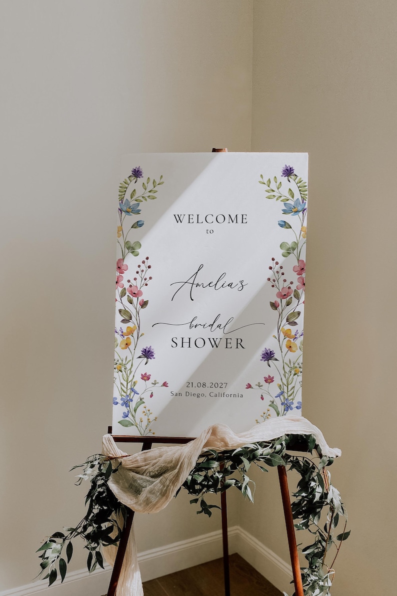May include: A white sign with a floral border and the text "Welcome to Amelia's bridal shower 21.08.2027 San Diego, California".
