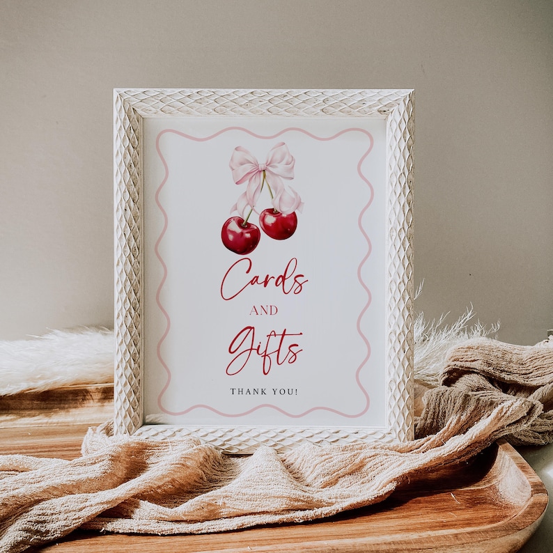 May include: White frame with a pink and white sign that says "Cards and Gifts" with a watercolour illustration of two cherries with a pink bow.