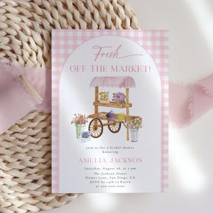 Può includere: Un invito a un baby shower rosa e bianco a quadretti con il testo "Fresh Off The Market!". L'invito presenta un'illustrazione ad acquerello di un carretto di fiori con vari fiori e il nome Amelia Jackson.