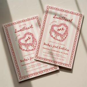 Peut inclure: Deux cartons d'invitation d'anniversaire à rayures roses et blanches. Les invitations présentent un motif de gâteau en forme de cœur avec le texte "one" au centre. Le texte indique "our little Sweetheart is turning one" et "Hailey's first birthday".