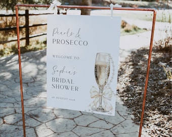 Puede incluir: Un cartel blanco con texto negro que dice "Pearls & Prosecco Bienvenida a la despedida de soltera de Sophia 28 de agosto de 2028". El cartel presenta una ilustración de acuarela de una copa de champán con un collar de perlas y un lazo blanco.