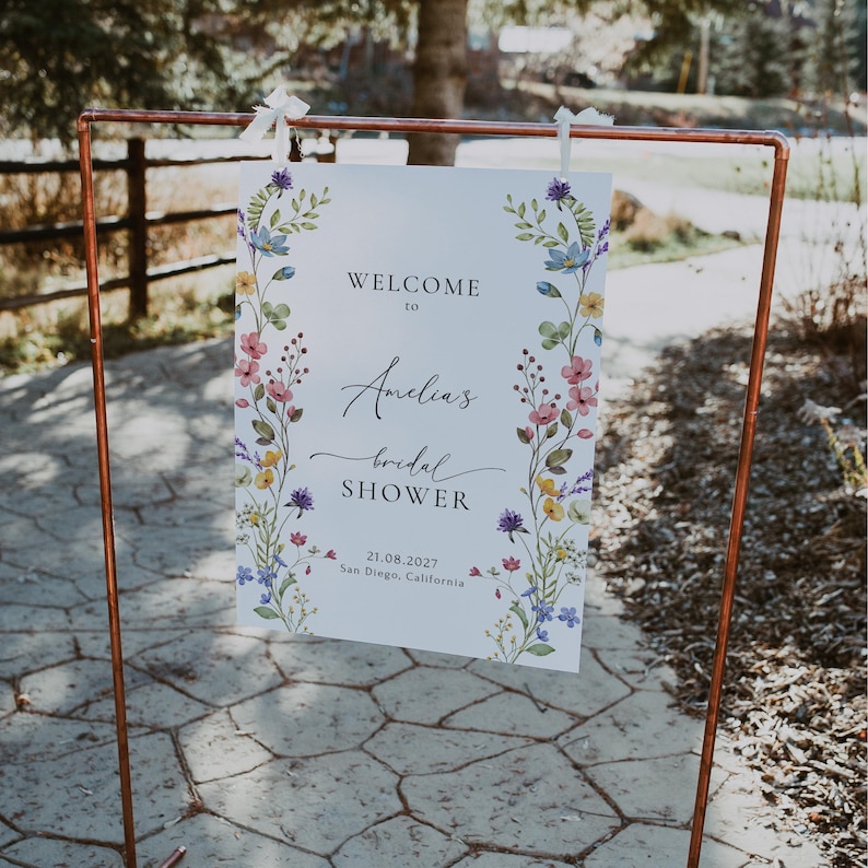 May include: A white sign with a floral border and the text "Welcome to Amelia's Bridal Shower 21.08.2027 San Diego, California".