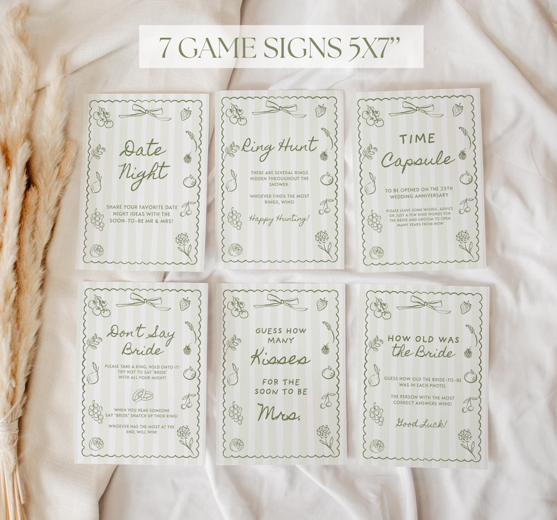 K&ouml;nnte beinhalten: Sieben 12,7 cm x 17,8 cm gro&szlig;e Spielschilder mit einem hellgr&uuml;nen und wei&szlig;en Streifendesign. Jedes Schild hat einen anderen Spieltitel, wie "Date Night" und "Ring Hunt", mit dekorativen Blumen- und Fruchtdarstellungen. Die Schilder sind f&uuml;r eine Hochzeit.