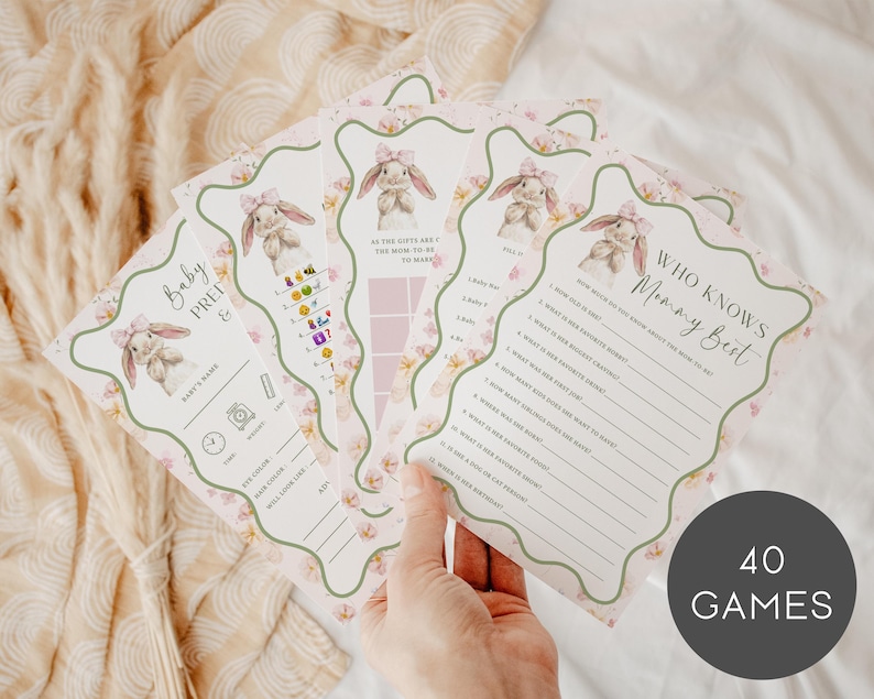 May include: A collection of baby shower game cards with a bunny theme. The cards feature illustrations of bunnies, floral accents, and various game prompts. The text "Baby Prep" and "Who Knows Mommy Best" are visible. The image includes a round graphic that says "40 GAMES".