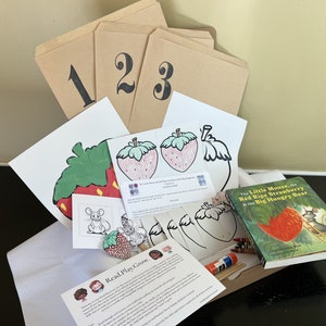 May include: A craft kit for kids featuring a book titled "The Little Mouse, the Red Ripe Strawberry & the Big Hungry Bear", coloring pages, and craft supplies. The kit includes a brown paper bag with the numbers 1, 2, and 3 printed on it.