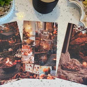 May include: Three autumn-themed postcards with warm, inviting imagery. One shows a cozy outdoor fire pit scene, another a collage with pumpkins and the text "Pumpkin Patch", and the third a cozy indoor scene with a cup of tea and a candle.