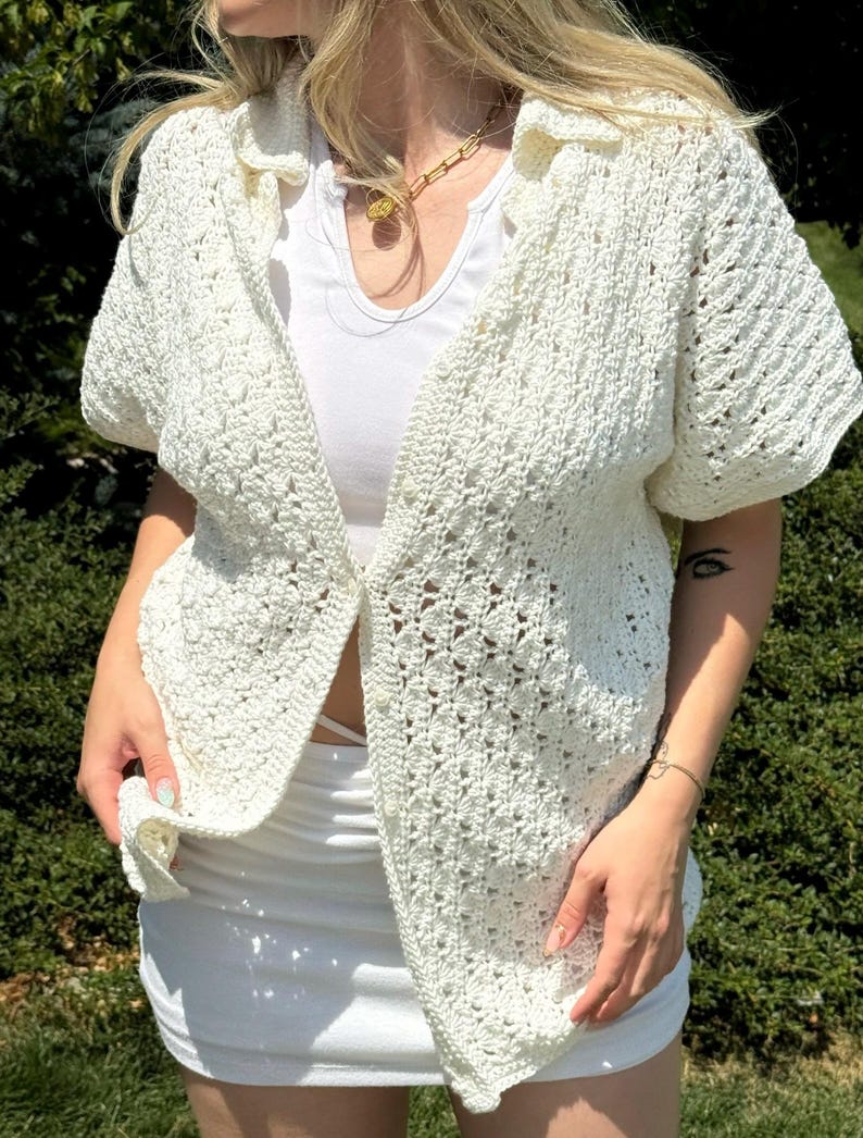 May include: A white crochet button-up shirt with short sleeves. The shirt has a delicate open-weave pattern.