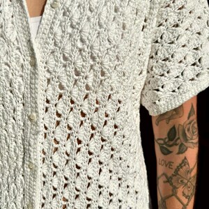 May include: White crochet button-up shirt with short sleeves. The shirt has a delicate, open-weave pattern.