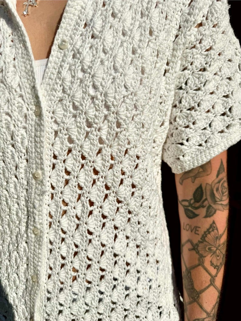 May include: White crochet button-up shirt with short sleeves. The shirt has a delicate, open-weave pattern.