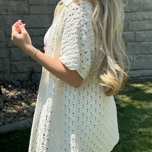 May include: A white crochet cardigan with a loose fit and short sleeves. The cardigan has a delicate openwork pattern.
