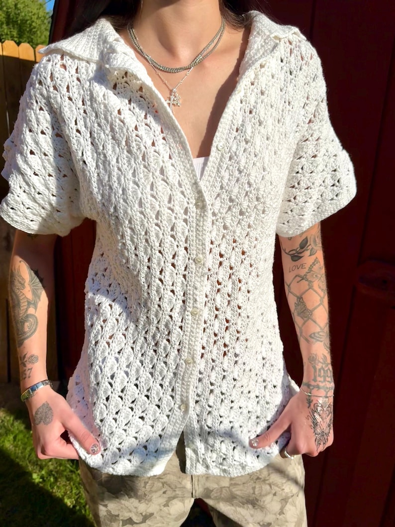 May include: White crochet button-up shirt with short sleeves. The shirt has a delicate openwork pattern.