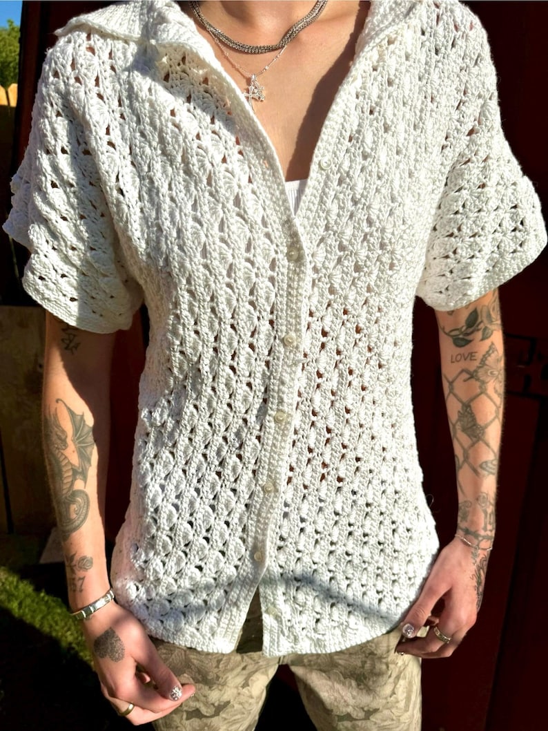 May include: White crochet button-up shirt with short sleeves. The shirt has a delicate open-weave pattern.