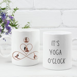 May include: Two white ceramic mugs with black text and illustrations. One mug features the text "It's Yoga O'Clock" and the other mug has a brown infinity symbol with four women in yoga poses.