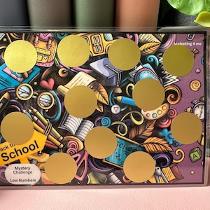 May include: A colorful back to school themed game board with gold circles that can be covered with stickers. The board has the text "Back to School" and "Mystery Challenge Low Numbers".