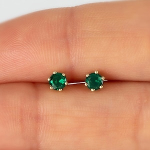 Op de afbeelding: Een paar gouden oorbelletjes met kleine, ronde, groene edelstenen.