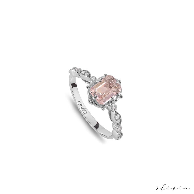 May include: A delicate silver ring with a pink gemstone surrounded by smaller diamonds. The ring has a delicate, ornate design.