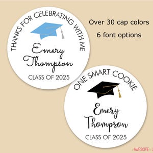 May include: Two round white graduation cookie labels with black text. The top label says "Thanks for celebrating with me" and the bottom label says "One smart cookie". Both labels feature a graduation cap, one blue and one black, and the name "Emery Thompson" and "Class of 2025".