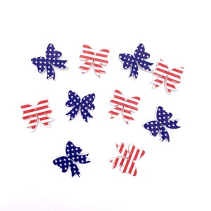 May include: Ten wooden bow-shaped ornaments with an American flag design. The bows are red, white, and blue with a star pattern.