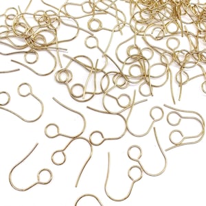 May include: A collection of gold-colored earring hooks, scattered across a white surface. The hooks have a simple, curved design with a loop at the top and a hook at the bottom, ideal for jewelry making and crafting.