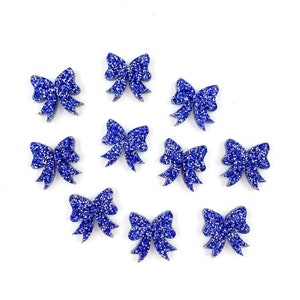 May include: Ten blue glitter bows with a silver shimmer. The bows are arranged in a circle on a white background.