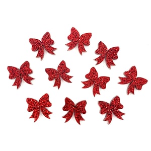 May include: Ten red glitter bows, each with a slightly different shape and size, are arranged on a white background.