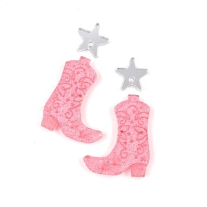Può includere: Due ciondoli a forma di stivali da cowboy rosa glitterati con ciondoli a forma di stella argentata glitterati.