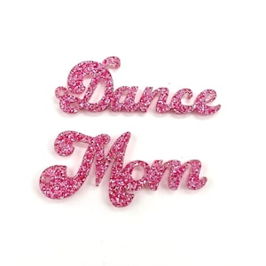 May include: Pink glitter acrylic words "Dance Mom" in a cursive font.