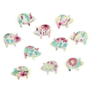 Könnte beinhalten: Zehn schwein-förmige Verzierungen mit floralen Mustern in Rosa, Blau und Grün. Die transparenten Verzierungen sind auf einer weißen Oberfläche verstreut. Jedes Schwein hat ein einzigartiges Blumenmuster.