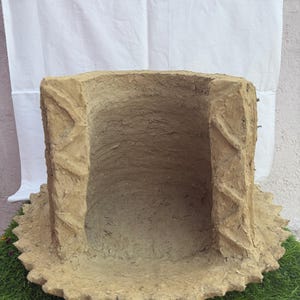 May include: A beige, rectangular planter with a textured finish. The sides feature a zigzag pattern, and the base has a scalloped edge. The interior is hollow. The planter is displayed on artificial green grass. The planter is likely made of clay.