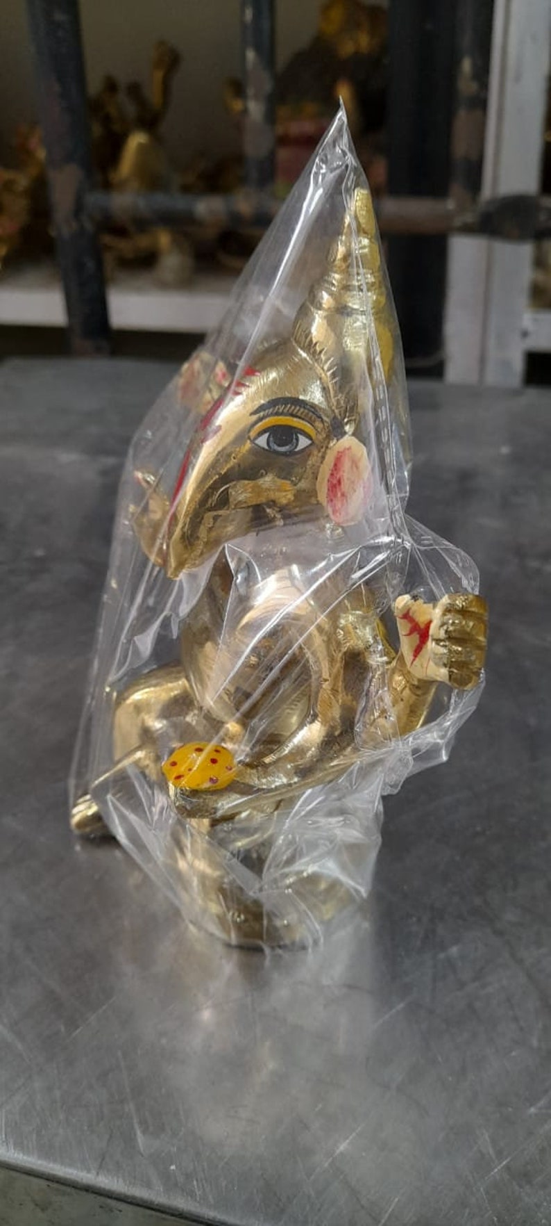 May include: A gold-colored Ganesha statue with red and yellow paint details, wrapped in clear plastic.