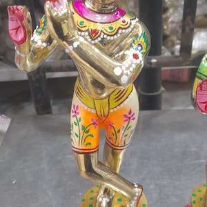 May include: A gold-coloured statue of a Hindu deity, painted with intricate details in pink, yellow, green, and white. The statue is standing on a red and pink lotus base.