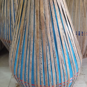 Puede incluir: Un tambor grande, redondo, azul y marrón con un diseño tejido. El tambor está hecho de madera y tiene una cabeza de cuero.