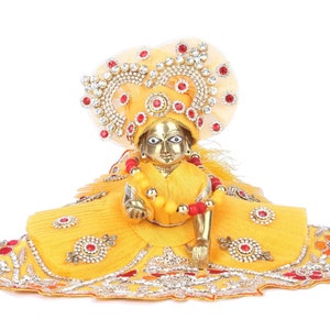 May include: A golden statue of a deity wearing a yellow and red embroidered outfit with a crown of jewels and a beaded necklace.