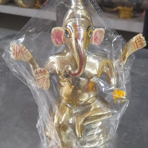 May include: A gold-colored statue of Ganesha, the Hindu god of wisdom and prosperity, with red and yellow accents. The statue is sitting on a base and has its trunk raised.