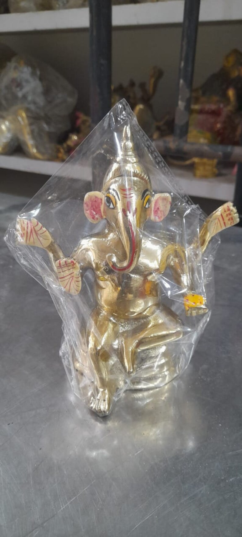 May include: A gold-colored statue of Ganesha, the Hindu god of wisdom and prosperity, with red and yellow accents. The statue is sitting on a base and has its trunk raised.