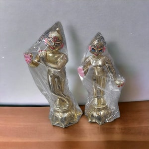 May include: Two gold-colored statues of deities, one male and one female, with painted details. The statues are standing on lotus-shaped bases and are wrapped in plastic.