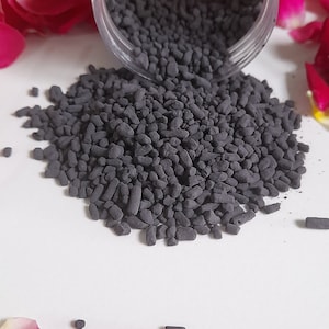 May include: A close-up of a small jar of black charcoal granules, surrounded by pink and yellow rose petals. The jar has a yellow label with the text "Gulab Incense".