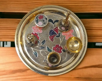 Puede incluir: Una bandeja redonda de latón con un diseño floral y cinco cuencos decorativos pequeños. Los cuencos son dorados y tienen una variedad de colores y patrones.